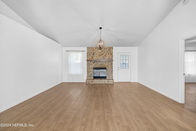 unfurnished living room featuring lofted ceiling, light hardwood / wood-style flooring, a fireplace, and an inviting chandelier