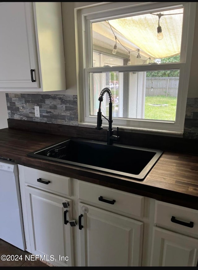 kitchen featuring white dishwasher, sink, backsplash, white cabinetry, and butcher block counters