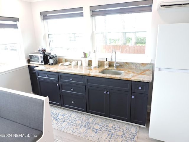 kitchen with light stone counters, sink, light wood-type flooring, an AC wall unit, and white refrigerator