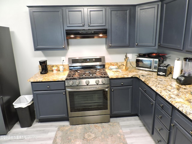 kitchen with appliances with stainless steel finishes, light stone counters, light hardwood / wood-style floors, and extractor fan