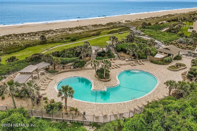 view of swimming pool with a water view, a view of the beach, and a patio