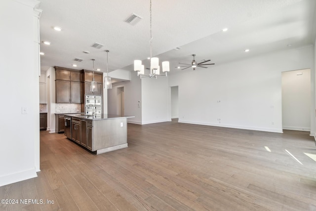 kitchen featuring hardwood / wood-style floors, a kitchen island with sink, ceiling fan with notable chandelier, hanging light fixtures, and dark brown cabinetry