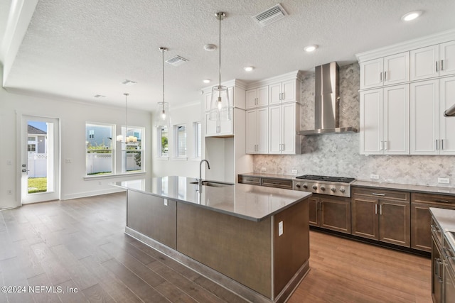 kitchen featuring sink, stainless steel gas cooktop, hanging light fixtures, a kitchen island with sink, and wall chimney range hood