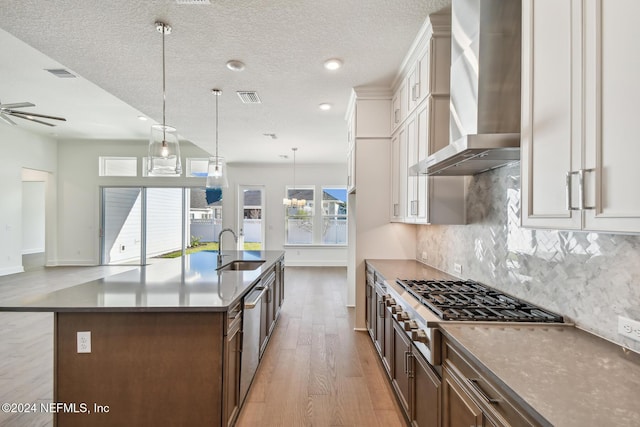 kitchen with sink, white cabinetry, a spacious island, decorative light fixtures, and wall chimney exhaust hood