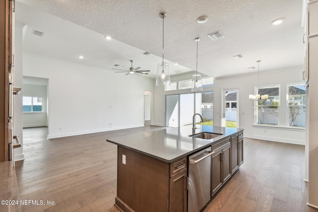 kitchen with dishwasher, wood-type flooring, sink, hanging light fixtures, and a center island with sink