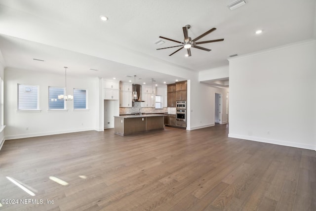 unfurnished living room with crown molding, sink, dark wood-type flooring, and ceiling fan with notable chandelier