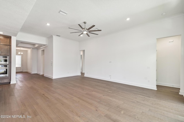 unfurnished living room with crown molding, ceiling fan with notable chandelier, and light hardwood / wood-style flooring