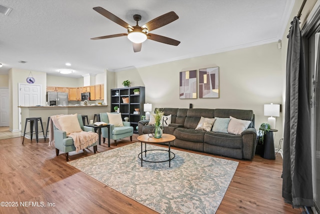 living room featuring light wood-type flooring, ceiling fan, and ornamental molding