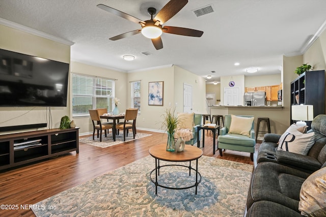 living room featuring ceiling fan, wood-type flooring, ornamental molding, and a textured ceiling