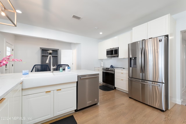 kitchen with appliances with stainless steel finishes, white cabinets, sink, and light wood-type flooring