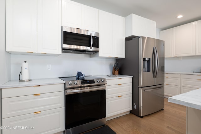 kitchen with light stone counters, appliances with stainless steel finishes, white cabinetry, and light wood-type flooring