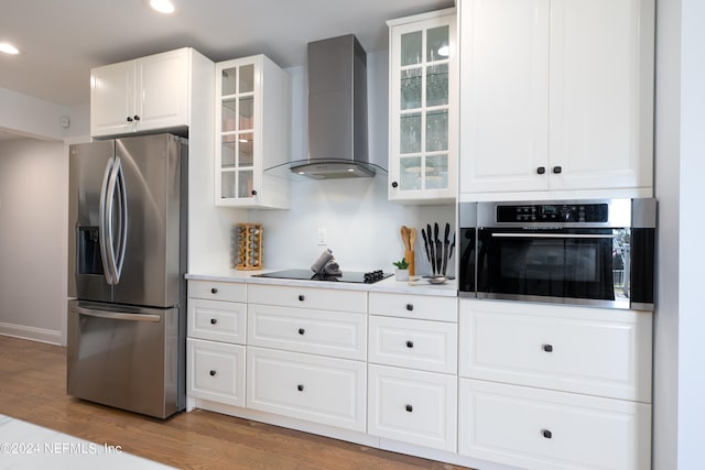 kitchen featuring stainless steel appliances, light wood-type flooring, wall chimney exhaust hood, and white cabinetry