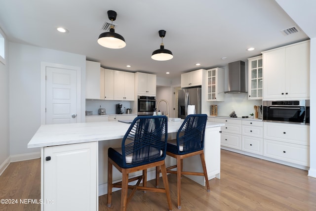 kitchen featuring stainless steel fridge with ice dispenser, light wood-type flooring, wall chimney range hood, and an island with sink