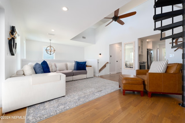 living room with ceiling fan with notable chandelier, a towering ceiling, and hardwood / wood-style flooring