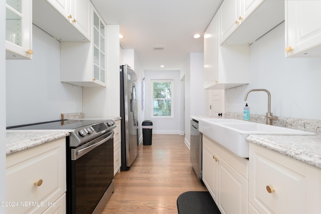 kitchen featuring light stone countertops, light wood-type flooring, white cabinetry, appliances with stainless steel finishes, and sink