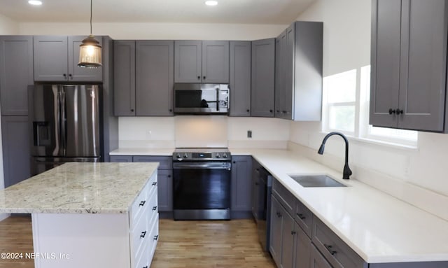 kitchen with a kitchen island, hanging light fixtures, stainless steel appliances, sink, and light wood-type flooring