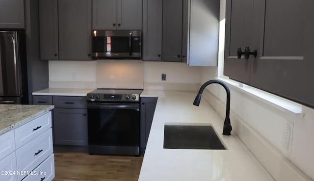 kitchen featuring wood-type flooring, light stone countertops, gray cabinetry, appliances with stainless steel finishes, and sink