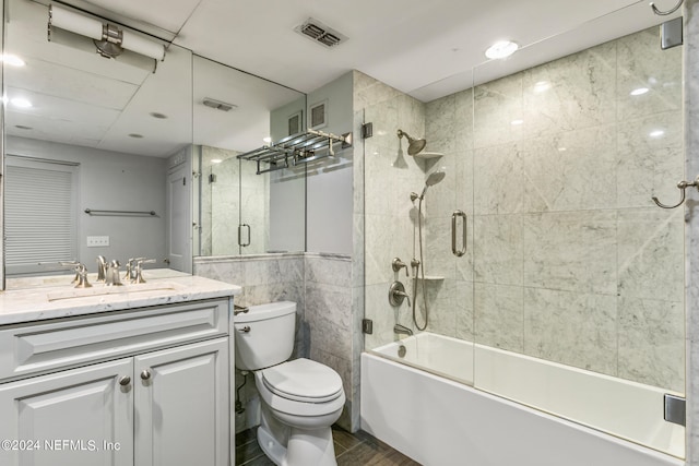 full bathroom with shower / bath combination with glass door, vanity, tile walls, and toilet