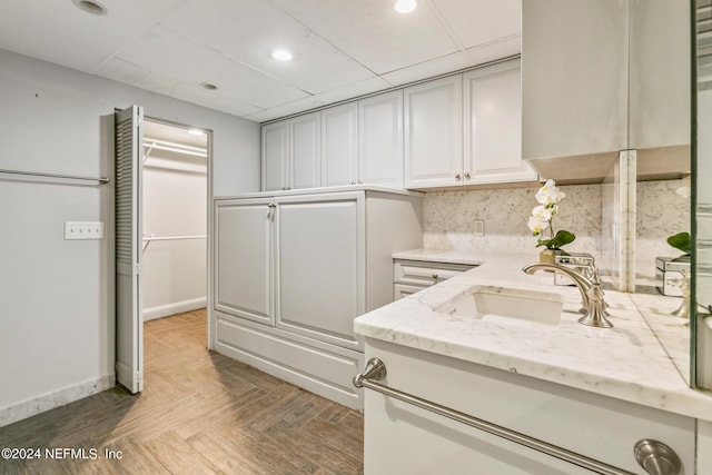 kitchen with a paneled ceiling, sink, light stone countertops, parquet flooring, and tasteful backsplash