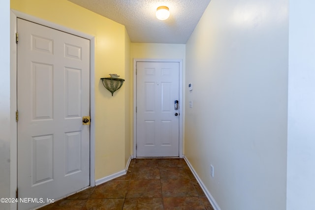 doorway to outside featuring a textured ceiling and dark tile flooring