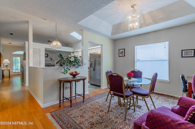 dining space featuring a raised ceiling, a chandelier, light hardwood / wood-style floors, and a textured ceiling