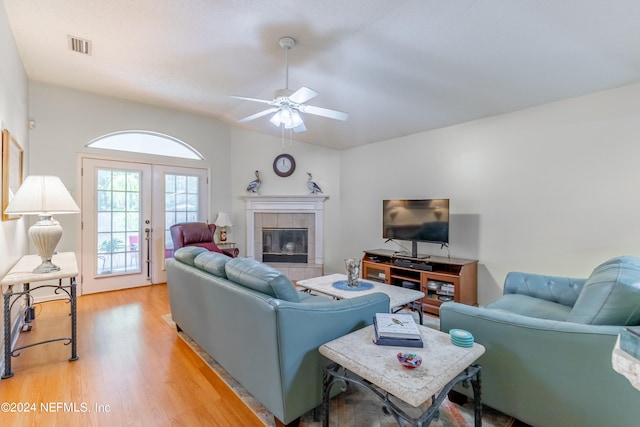 living room with french doors, a tiled fireplace, ceiling fan, and light hardwood / wood-style flooring