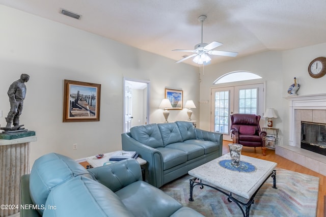 living room featuring vaulted ceiling, ceiling fan, hardwood / wood-style floors, a tile fireplace, and french doors