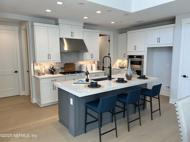 kitchen with stainless steel appliances, light wood-style flooring, white cabinets, a sink, and under cabinet range hood