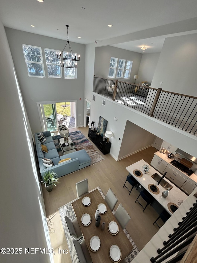 living room with a wealth of natural light, a notable chandelier, a towering ceiling, and wood finished floors