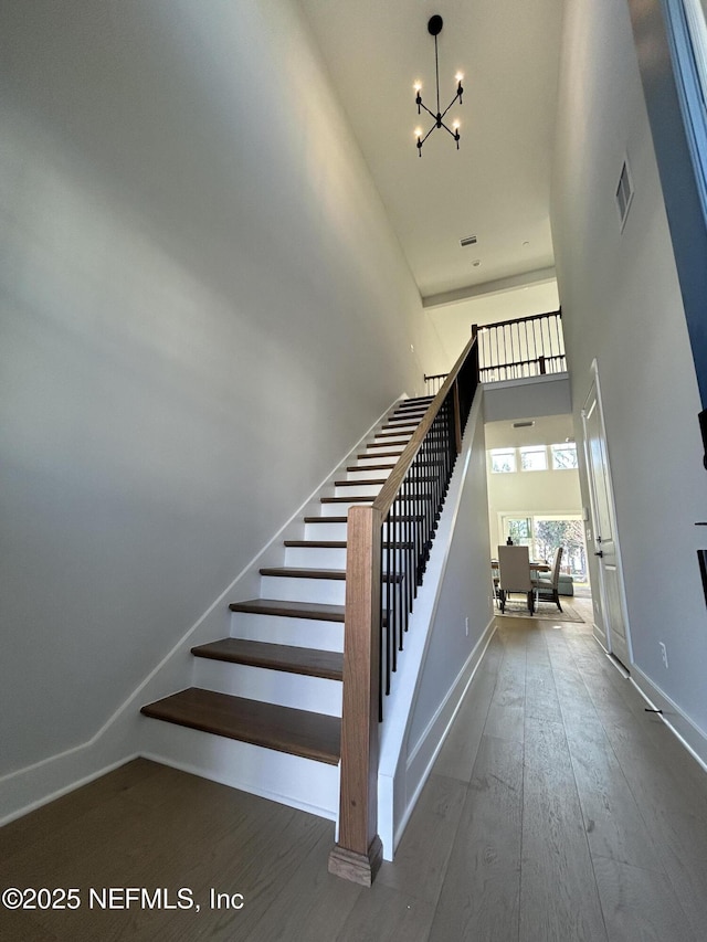 staircase with a towering ceiling, an inviting chandelier, visible vents, and wood finished floors