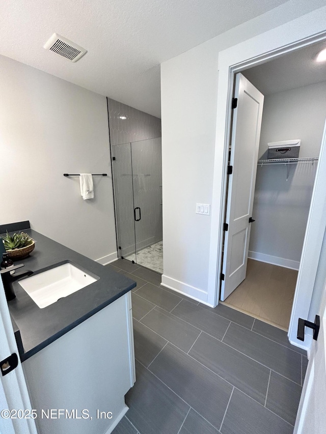 full bathroom with a walk in closet, visible vents, a shower stall, and baseboards