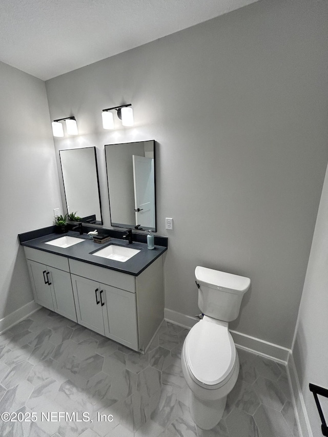 bathroom with marble finish floor, a sink, toilet, and baseboards