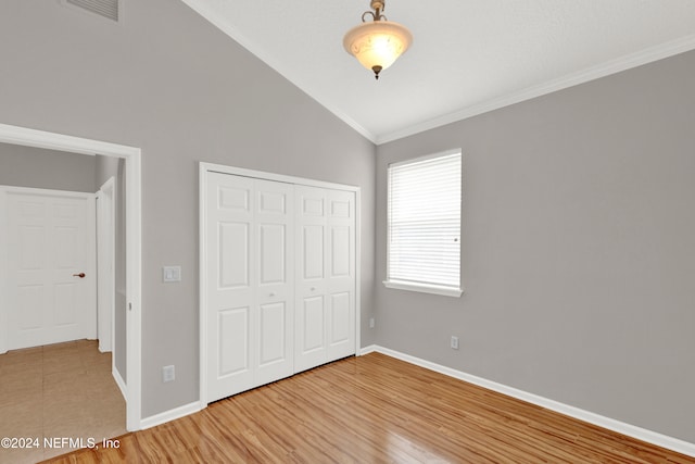 unfurnished bedroom with lofted ceiling, wood-type flooring, crown molding, and a closet