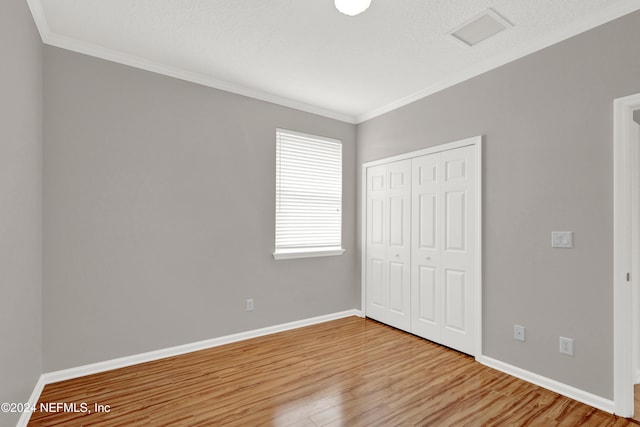 unfurnished bedroom with a textured ceiling, hardwood / wood-style flooring, a closet, and ornamental molding