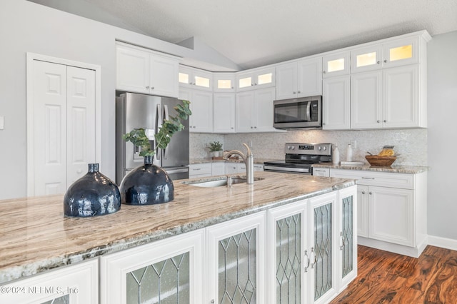 kitchen with stainless steel appliances, sink, vaulted ceiling, white cabinets, and tasteful backsplash