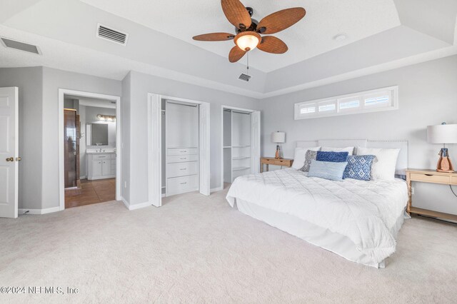 bedroom with light carpet, connected bathroom, a raised ceiling, and ceiling fan