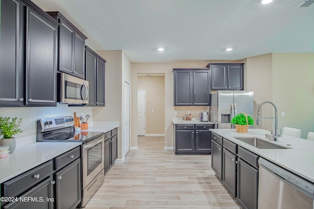 kitchen with a textured ceiling, light wood-type flooring, stainless steel appliances, and sink