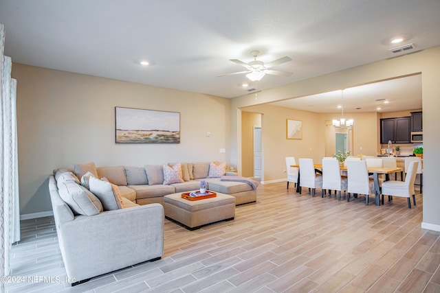 living room featuring ceiling fan with notable chandelier and light hardwood / wood-style flooring