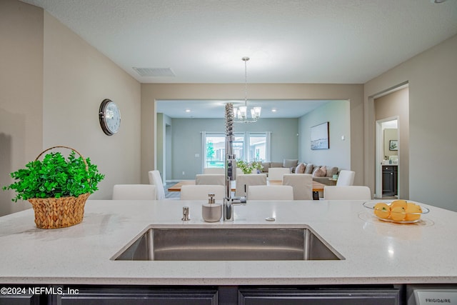 kitchen featuring pendant lighting, sink, a notable chandelier, light stone counters, and dishwashing machine