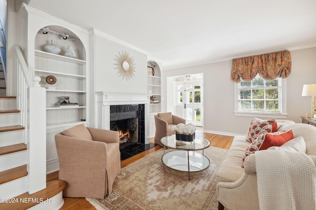 living room with a high end fireplace, built in shelves, light hardwood / wood-style flooring, and ornamental molding