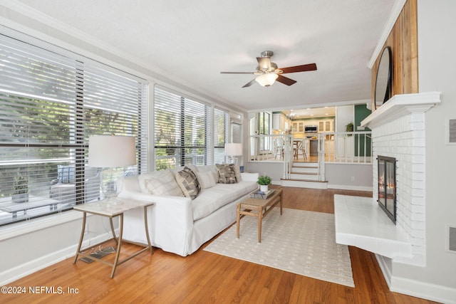 living room with hardwood / wood-style floors, a brick fireplace, ceiling fan, and ornamental molding