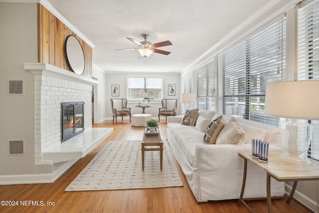 living room featuring hardwood / wood-style flooring, ceiling fan, a fireplace, and crown molding