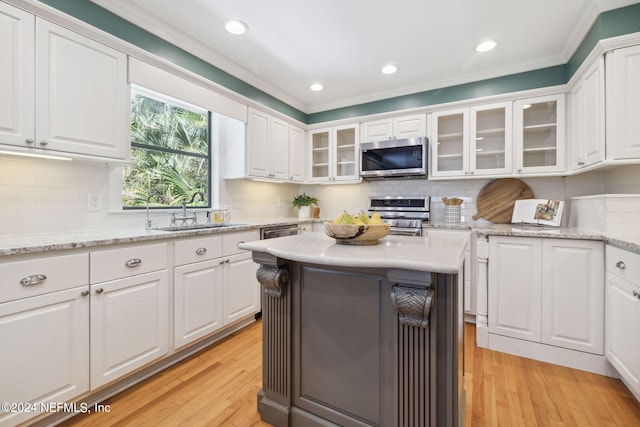 kitchen with white cabinets, sink, crown molding, appliances with stainless steel finishes, and light hardwood / wood-style floors