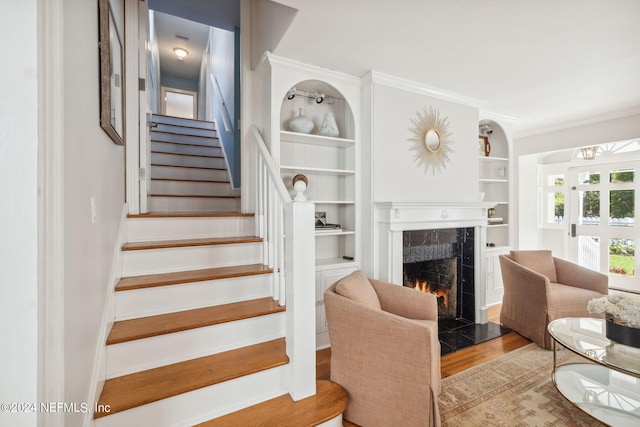 staircase with hardwood / wood-style flooring, built in shelves, crown molding, and a fireplace