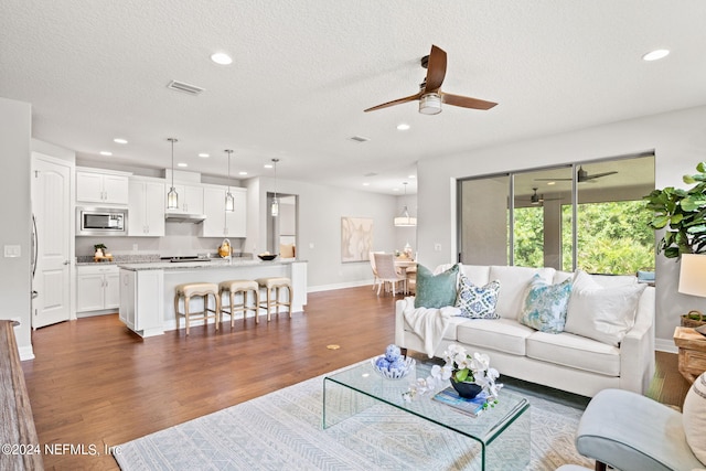 living room with ceiling fan, a textured ceiling, and dark hardwood / wood-style flooring