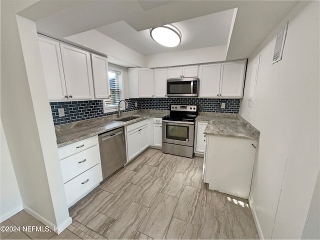 kitchen with appliances with stainless steel finishes, sink, backsplash, white cabinetry, and light stone countertops