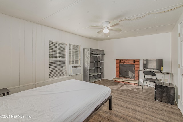 bedroom featuring a brick fireplace, wood-type flooring, and ceiling fan