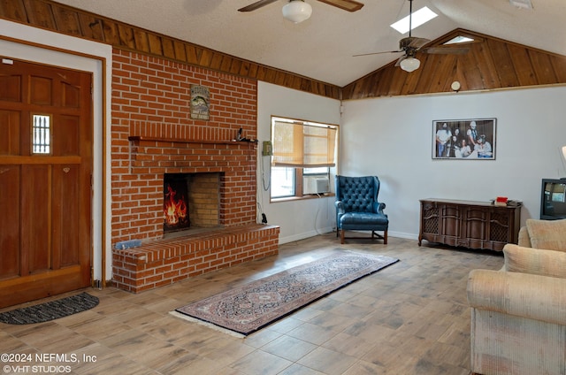 living room with ceiling fan, a textured ceiling, vaulted ceiling with skylight, and a fireplace