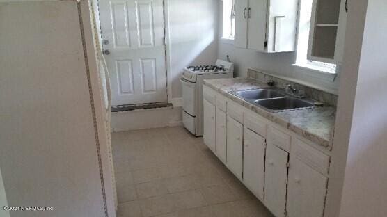 kitchen with sink, white appliances, white cabinetry, and light tile floors