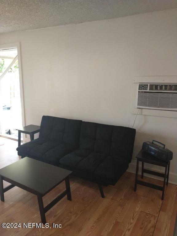 living room with a wall mounted AC, hardwood / wood-style flooring, and a textured ceiling